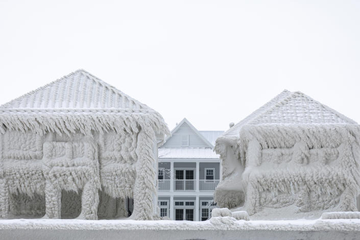 海岸にある完全に霜で覆われた 2 つの家屋の後ろに、通りの反対側の家が見えます。雪は最小限しか残っていません。