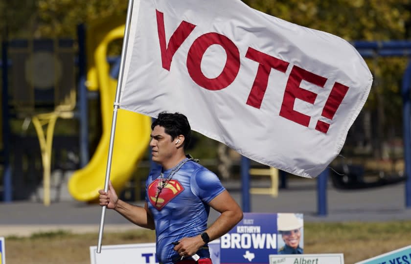 A jogger carries a Vote! flag as he passes a polling station, Tuesday, Nov. 3, 2020, in San Antonio.