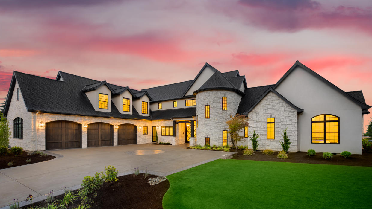 facade of home with manicured lawn, and backdrop of trees and dark blue sky.