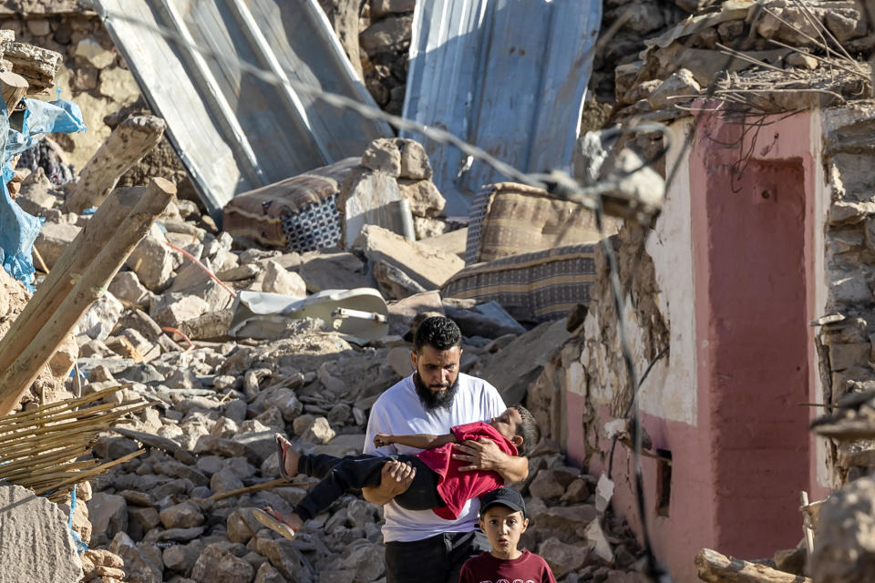 A man carries a child as he walks past destroyed houses after an earthquake in the mountain village of Tafeghaghte, southwest of Marrakech, Morocco, on Sept. 9, 2023. / Credit: FADEL SENNA/AFP via Getty Images