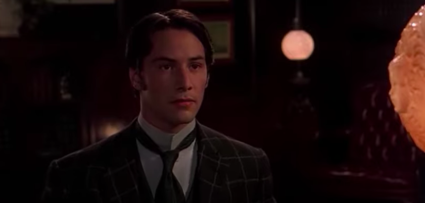 A man in period piece garb sits at a desk