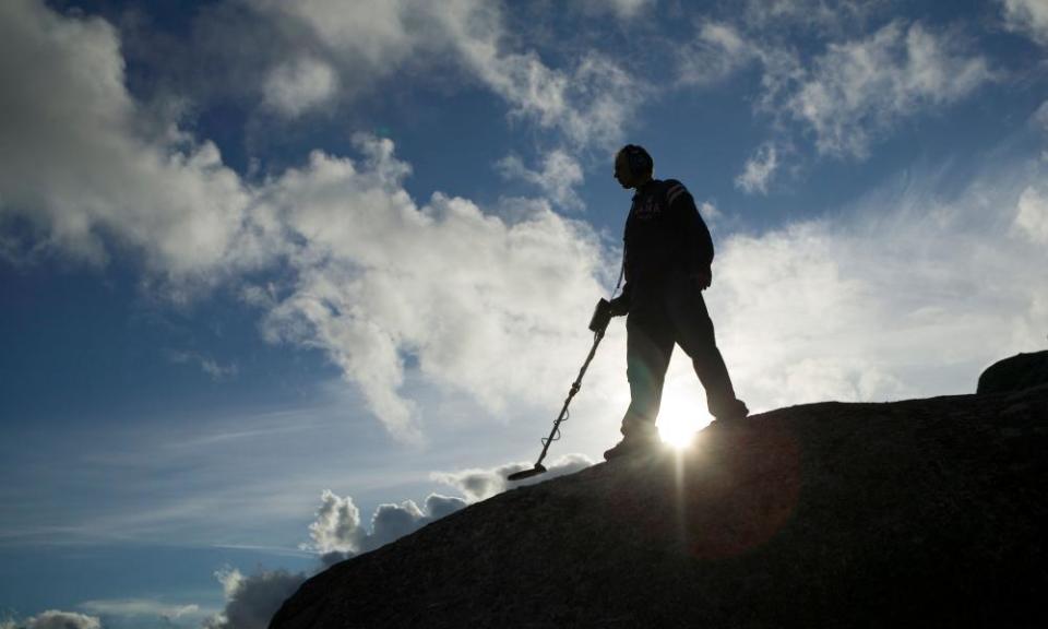 Man with metal detector silhouetted against  blue sky