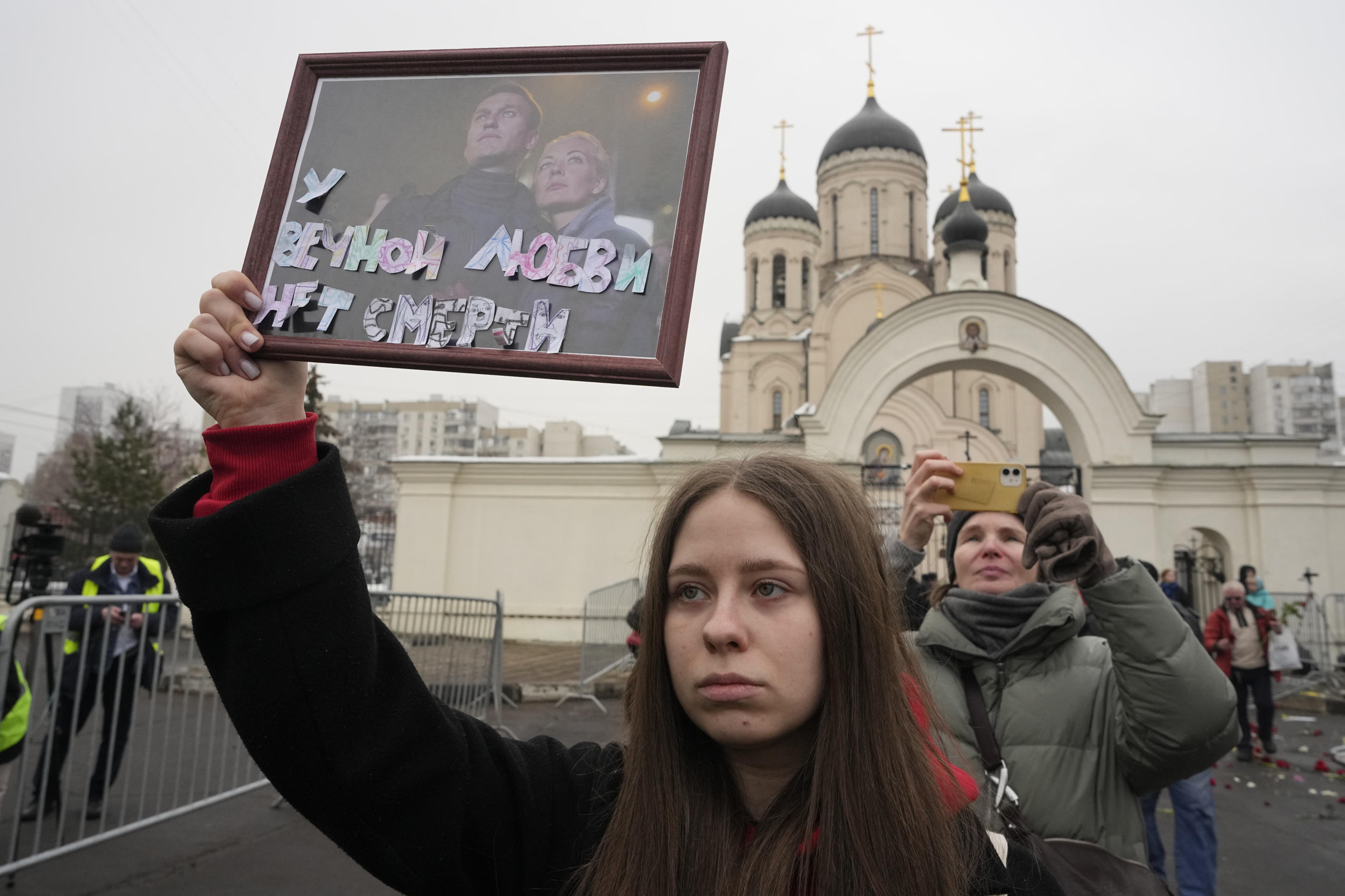 A woman holds up a framed portrait of Alexei Navalny and his wife, Yulia Navalnaya, outside the church in Moscow.