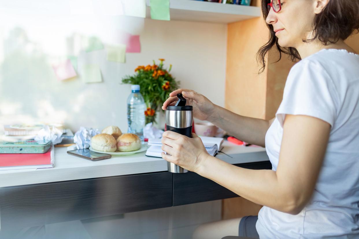 woman at desk ready to drink from travel mug