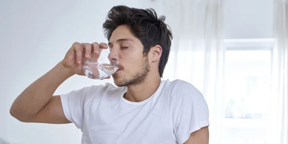man sitting in bed drinking water