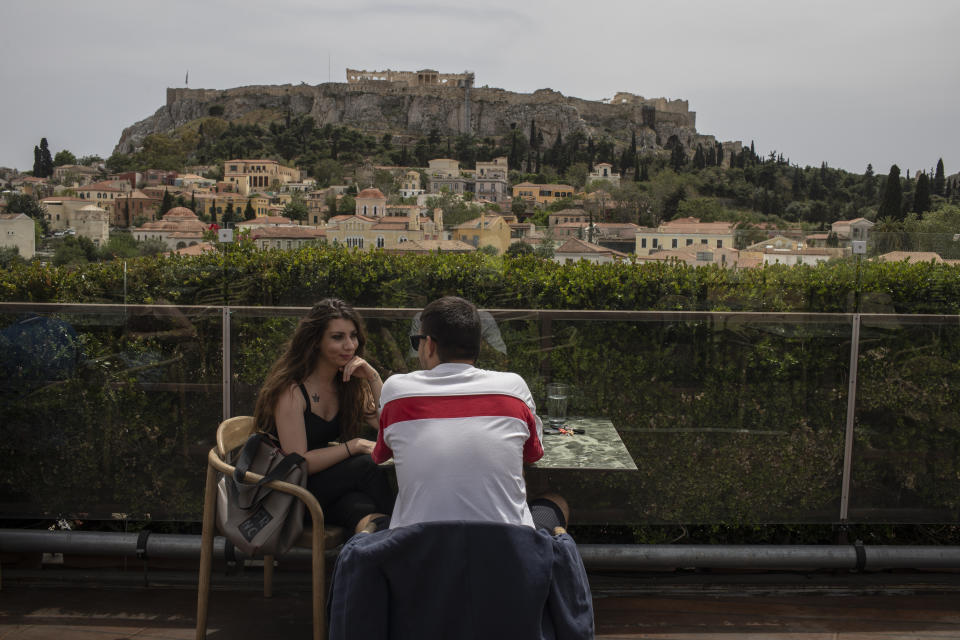 A man and a woman drink coffee in the Monastiraki district of Athens,with the ancient Acropolis hill in the background, Monday, May 3, 2021. Cafes and restaurants have reopened in Greece for sit-down service for the first time in nearly six months, as the country began easing coronavirus-related restrictions with a view to opening to the vital tourism industry in the summer. (AP Photo/Petros Giannakouris)