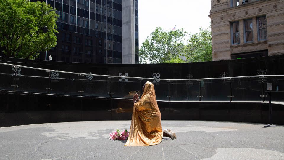 A golden cape Faustine wears in photos serves to represent the feminine divine, an energy that promotes positive change in the world and serves to protect sites that carry the legacies of the enslaved. Pictured above, Faustine poses at the African Burial Ground National Monument in downtown Manhattan. - Nona Faustine/Courtesy Brooklyn Museum