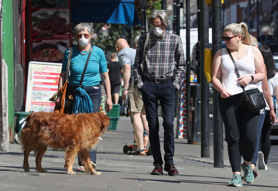 People wearing face masks walk past closed shops in Haringey, London, after the introduction of measures to bring the country out of lockdown.