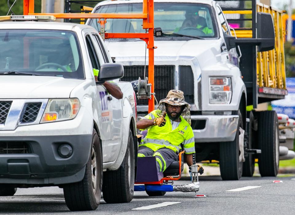 Marcell Coke, TRP Construction Group employee, gives a thumbs up to the driver of the pickup truck to go to the next reflector while replacing Raised Pavement Markers (RPMs) along East Silver Springs Boulevard last month. [Doug Engle/Ocala Star Banner]2021