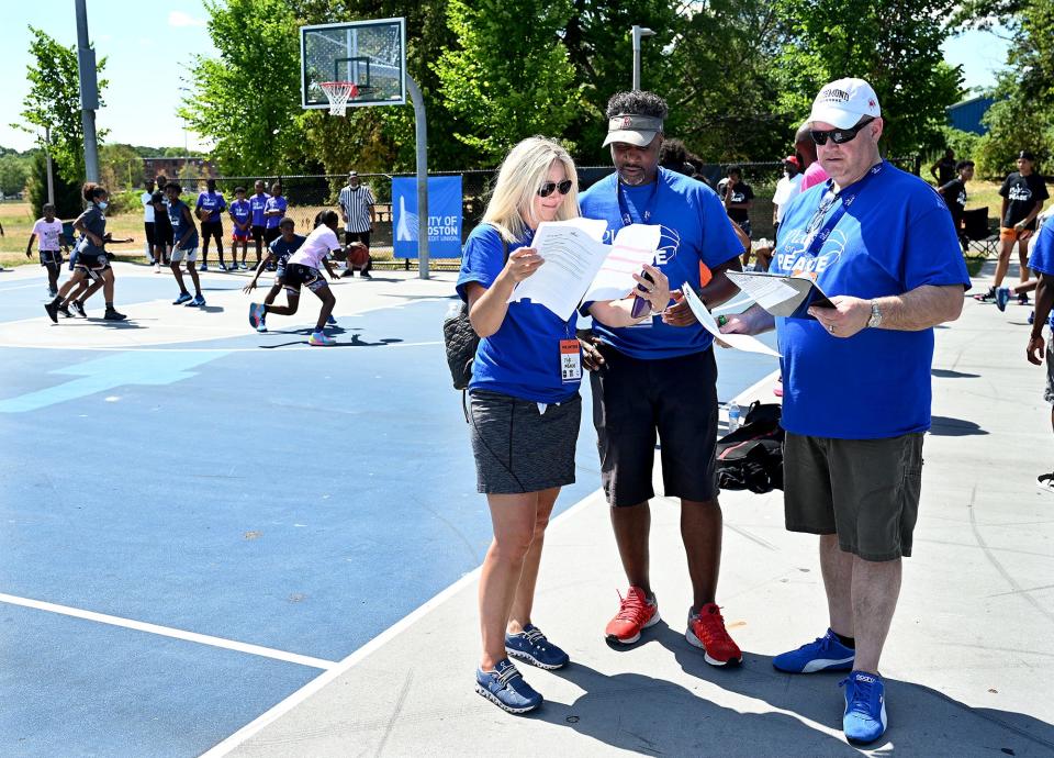 Lauren Mahoney, left, Philip Hillman and Andrew Surwilo, all friends from Lincoln-Sudbury High School Class of 1988, confer while helping to run the tournament they helped found, the "Play 4 Peace" 3-on-3 basketball tournament at Harambee Park in Boston on July 30.