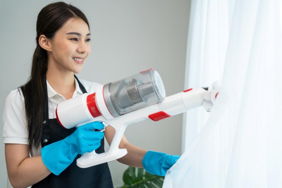 Woman using a hand-held vacuum on curtains