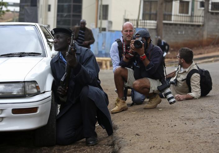 A policeman and photographers take cover after hearing gun shots near the Westgate shopping centre in Nairobi September 23, 2013. Thick smoke poured from the besieged Nairobi mall where Kenyan officials said their forces were closing in on Islamists holding hostages on Monday, three days after a raid by Somalia's al Shabaab killed at least 62 people. It remained unclear how many gunmen and hostages were still cornered in the Westgate shopping centre, two hours after a series of loud explosions and gunfire were followed by a plume of black smoke, that grew in volume from one part of the complex. REUTERS/Karel Prinsloo (KENYA - Tags: CIVIL UNREST MEDIA TPX IMAGES OF THE DAY)