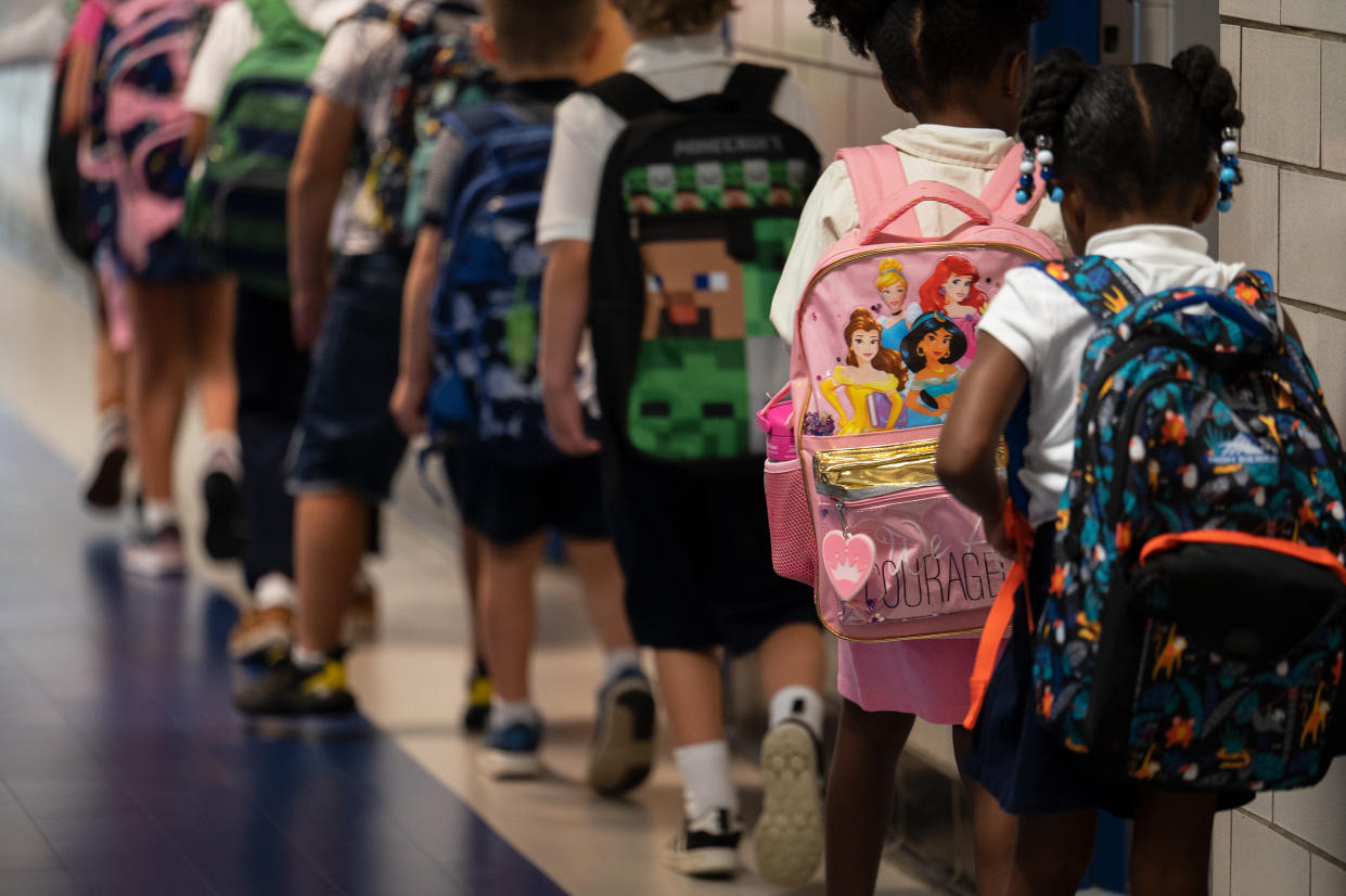 A line of schoolchildren from behind, showing an array of backpacks.