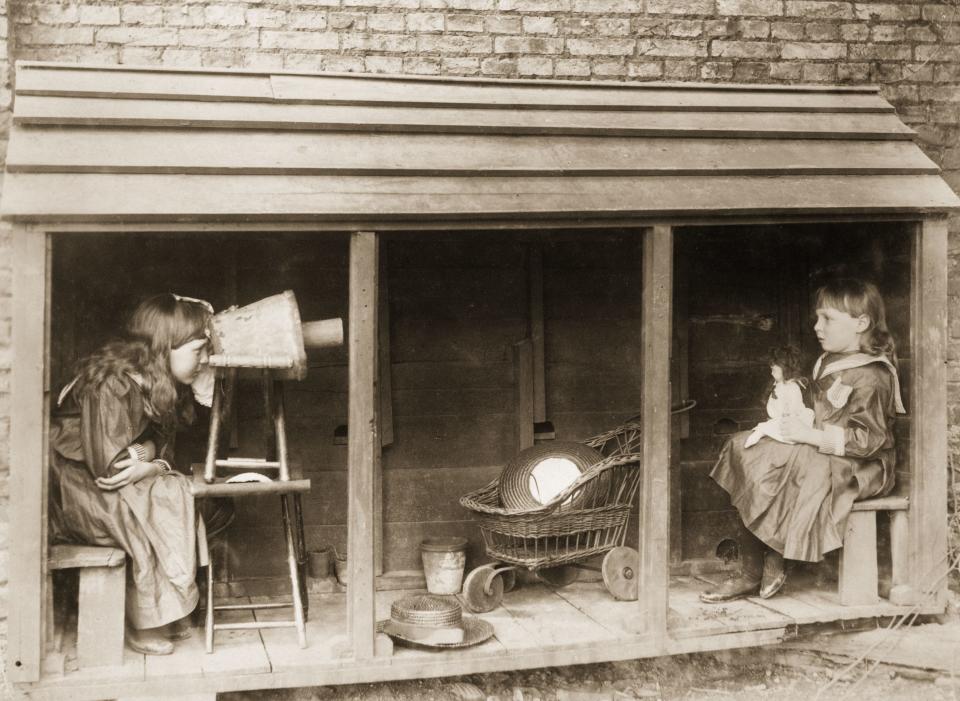 1887:  A little girl uses a camera made from a stool and a flowerpot to 'photograph' her friend.  (Photo by Rev F. C. Lambert/Hulton Archive/Getty Images)