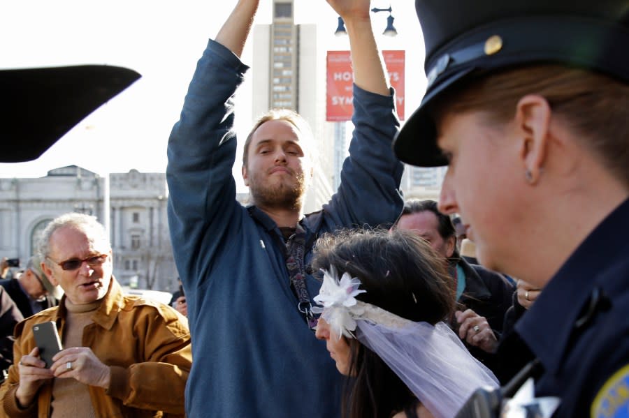 David DePape, center, records Gypsy Taub being led away by police after her nude wedding outside City Hall on Dec. 19, 2013, in San Francisco. DePape is accused of breaking into House Speaker Nancy Pelosi’s California home and severely beating her husband with a hammer. DePape was known in Berkeley, Calif., as a pro-nudity activist who had picketed naked at protests against local ordinances requiring people to be clothed in public. (AP Photo/Eric Risberg)