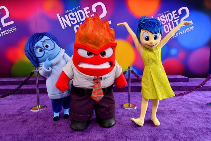 Joy, Sadness, Anger mascots from Disney-Pixar's Inside Out 2 at the world premiere, standing on a purple carpet with a backdrop that reads "Inside Out 2."