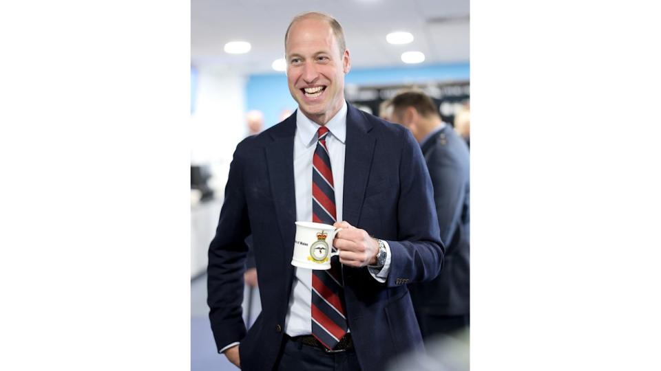 Prince William in a suit holding a mug