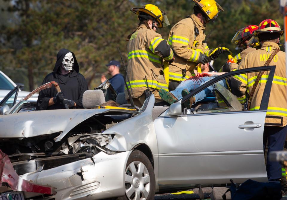 The Grim Reaper, played by Springfield Police Officer Matt Newton, left, stands watch as first responders with Mohawk Valley Rural Fire Department extract Mohawk High School student Hanna VanderPloeg, 16, from a damaged vehicle during a mock crash scene involving an impaired driver on Tuesday, Oct. 18, 2022.