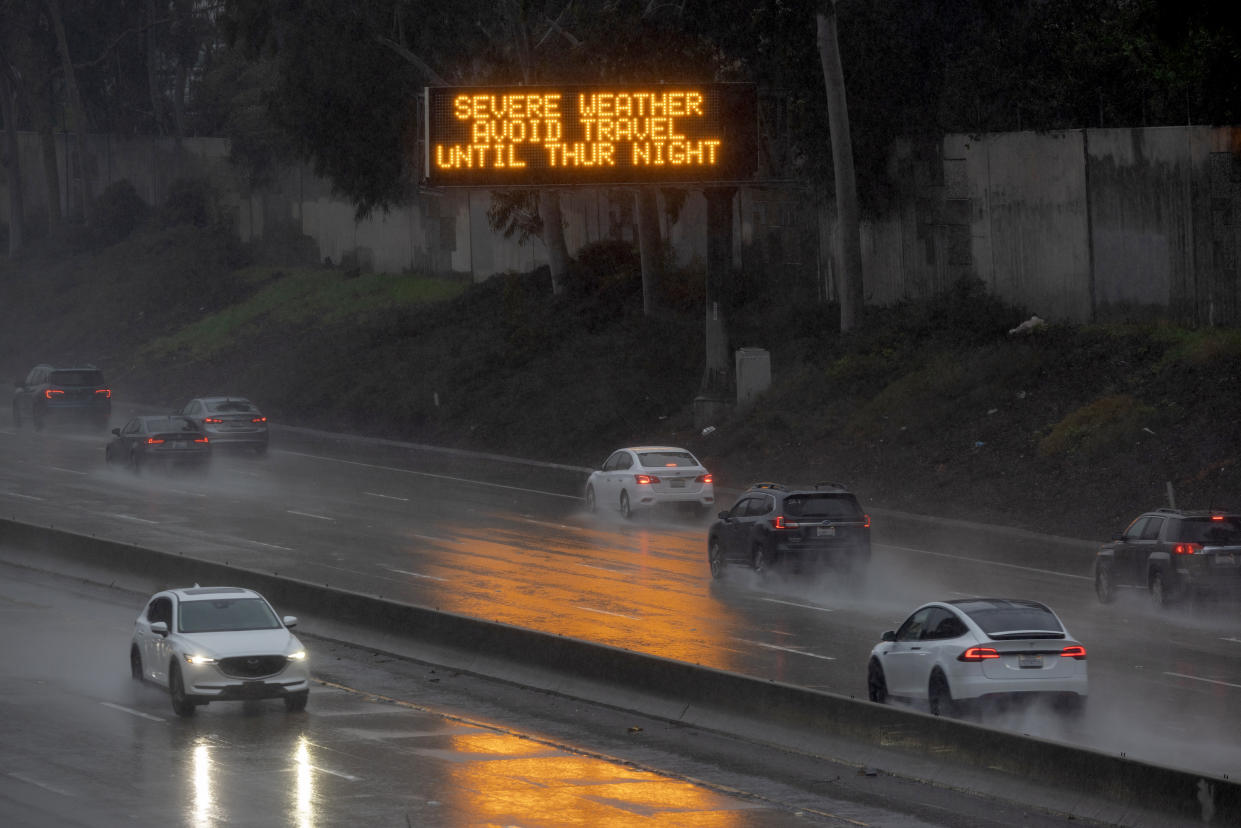 Motorists on a wet freeway drive past a sign reading: Severe weather. Avoid travel.