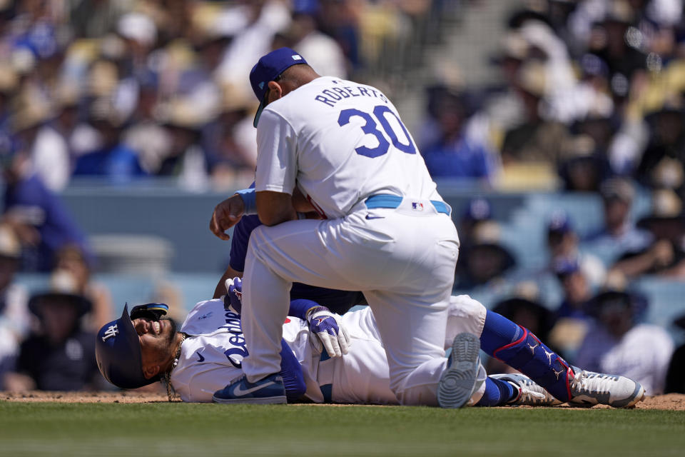 Los Angeles Dodgers' Mookie Betts, left, writhes on the ground after being hit by a pitch as manager Dave Roberts and a trainer tend to him during the seventh inning of a baseball game against the Kansas City Royals Sunday, June 16, 2024, in Los Angeles. (AP Photo/Mark J. Terrill)