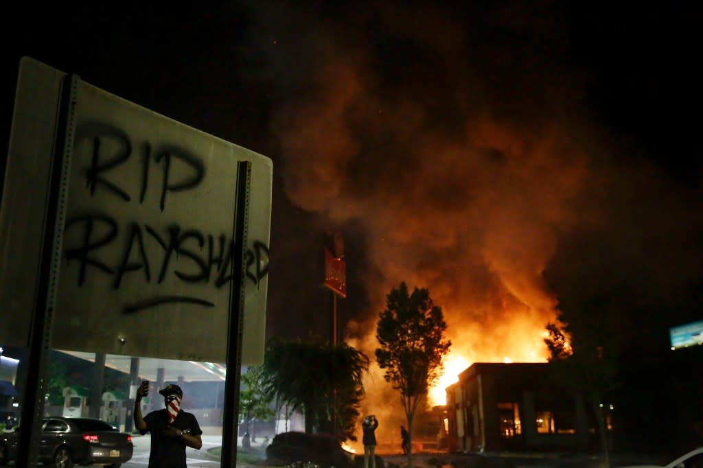 In this June 13, 2020 file photo, “RIP Rayshard” is spray-painted on a sign as flames engulf a Wendy’s restaurant where Rayshard Brooks was shot and killed by police in Atlanta. (AP Photo/Brynn Anderson, File)