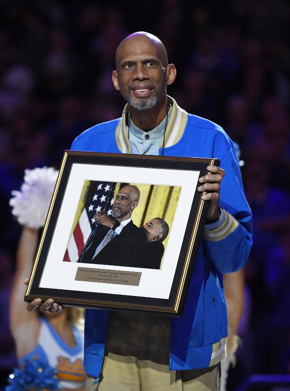 Kareem Abdul-Jabbar holds up a picture of himself receiving the Presidential Medal of Freedom from President Obama during halftime of an NCAA college basketball game between UCLA and Arizona, Saturday, Jan. 21, 2017, in Los Angeles. Abdul-Jabbar received the framed picture during a ceremony to celebrate Kareem Abdul-Jabbar day at UCLA. (AP Photo/Mark J. Terrill)