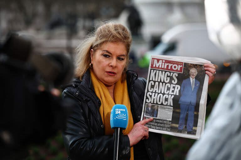 Una periodista frente al Palacio de Buckingham muestra la tapa del Mirror con la noticia del cáncer del rey Carlos III. (HENRY NICHOLLS / AFP)