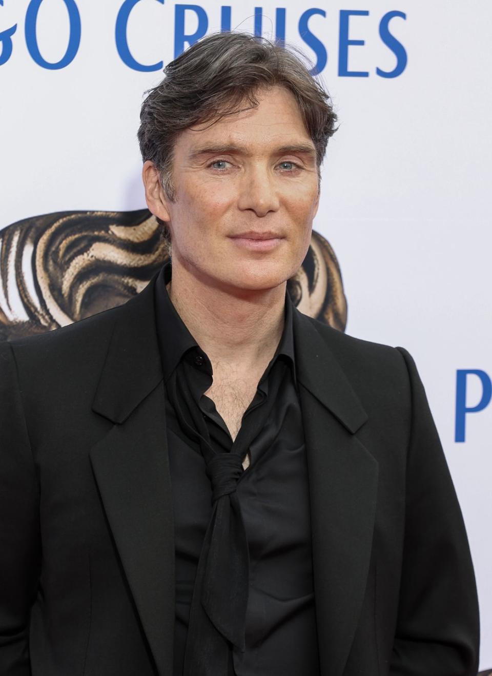 cillian murphy looks at the camera while wearing a black suit jacket, shirt, and tie