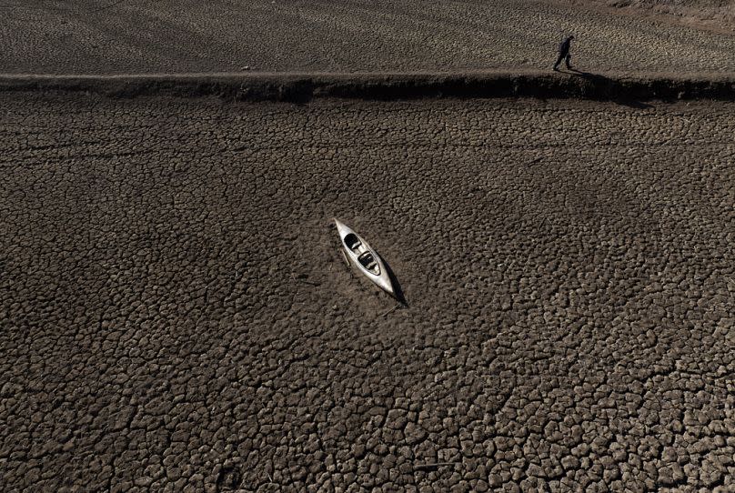 A man walks past an abandoned canoe at the Sau reservoir, which is only at 5 percent of its capacity, in Vilanova de Sau