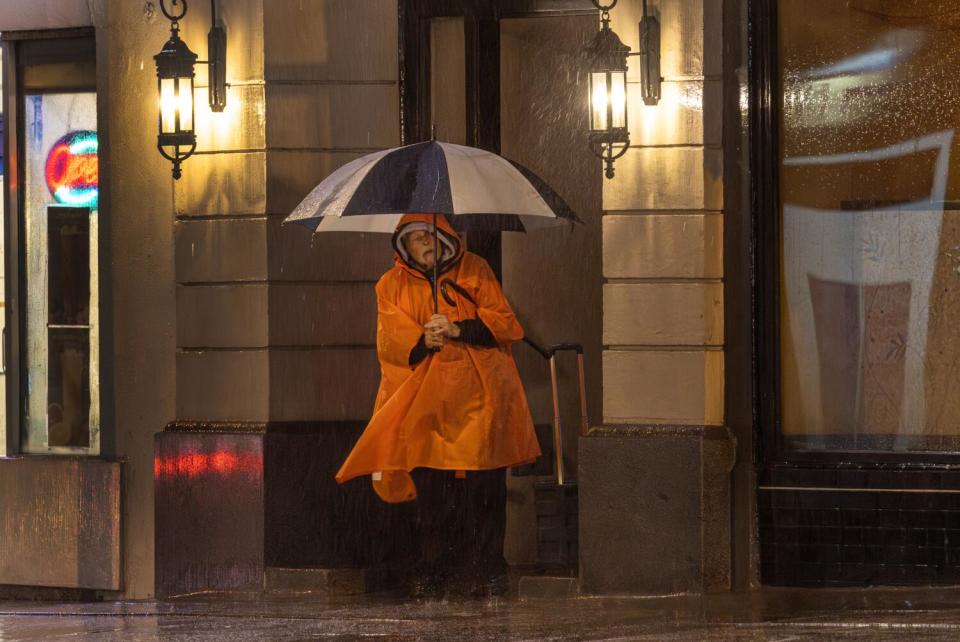 A pedestrian huddles in a doorway as heavy rain falls on Colorado Boulevard in Pasadena Sunday night.