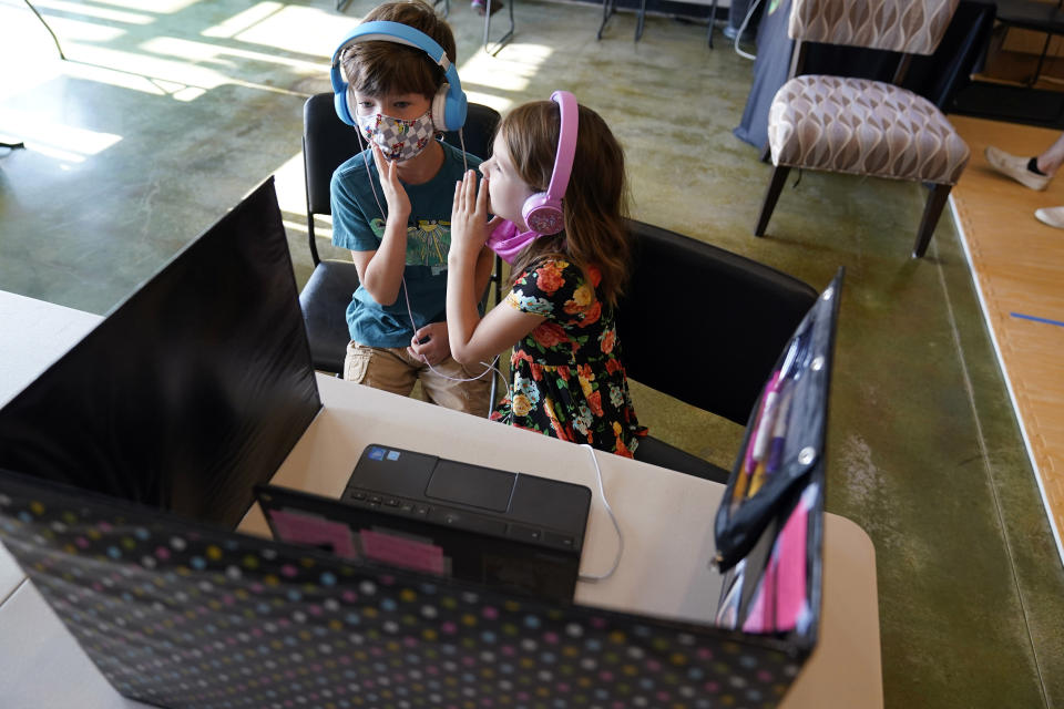 FILE - Audra Quisenberry, right, whispers in the ear of her classmate, Logan Bowhay, both 6, as they wait to meet other schoolmates via online Zoom, at Premier Martial Arts, Aug. 24, 2020, in Wildwood, Mo. In interviews with The Associated Press, close to 50 school leaders, teachers, parents and health officials reflected on decisions to keep students in extended online learning, especially during the spring semester of 2021. (AP Photo/Jeff Roberson, File)