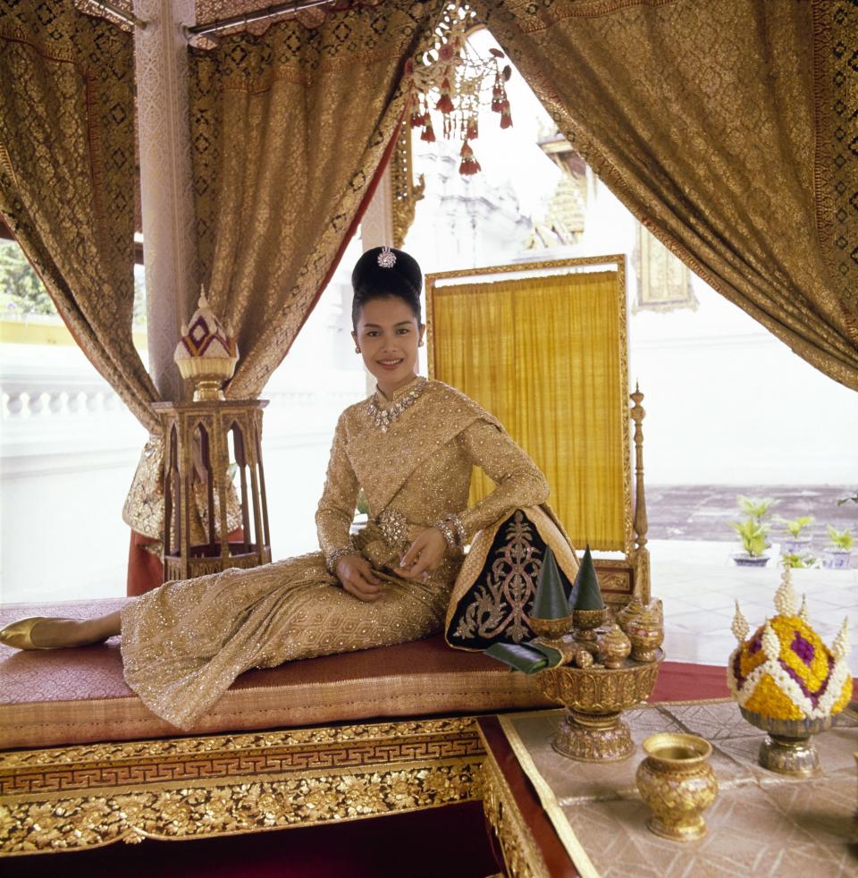 “H. M. Queen Sirikit of Thailand: On a gold-leafed Thai bed in the King’s coronation pavilion, Queen Sirikit in a dress of twenty-carat gold embossed in crystal, appears to be paved in diamonds. . . . This court dress, which the Queen wore to the Greek Royal wedding, was created for her by Pierre Balmain, who designs her superb Paris and Bangkok clothes, her shoes, her Royal umbrellas.”