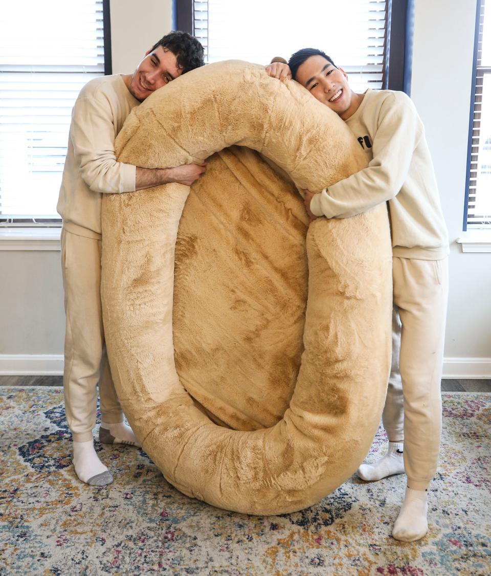 Noah Silverman and Yuki Kinoshita with one of the founders of Plufl, shows the human-sized dog bed can be used. The pair have been featured on Shark Tank for their idea. December 2022