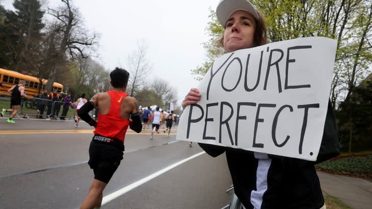 A woman holds up a sign that says You're Perfect