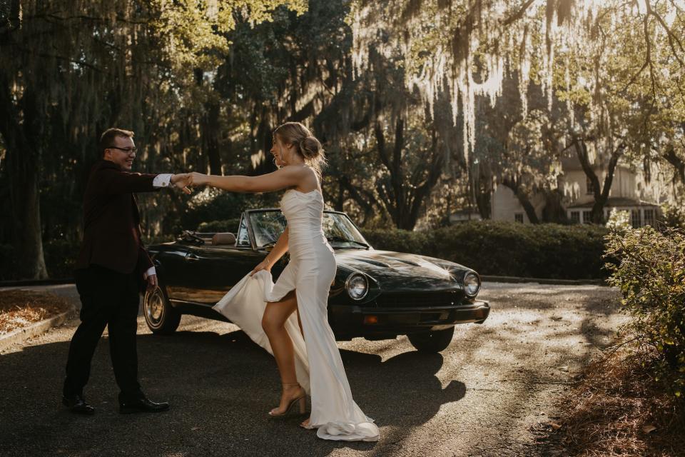 A bride and groom dance together in their wedding attire in front of a convertible.