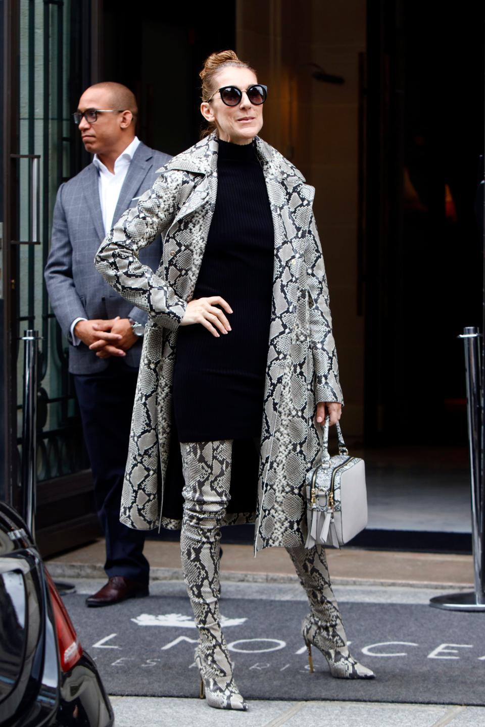 Celine in a snakeskin coat and matching thigh-high boots and a bag. She's wearing a black dress underneath and sunglasses.