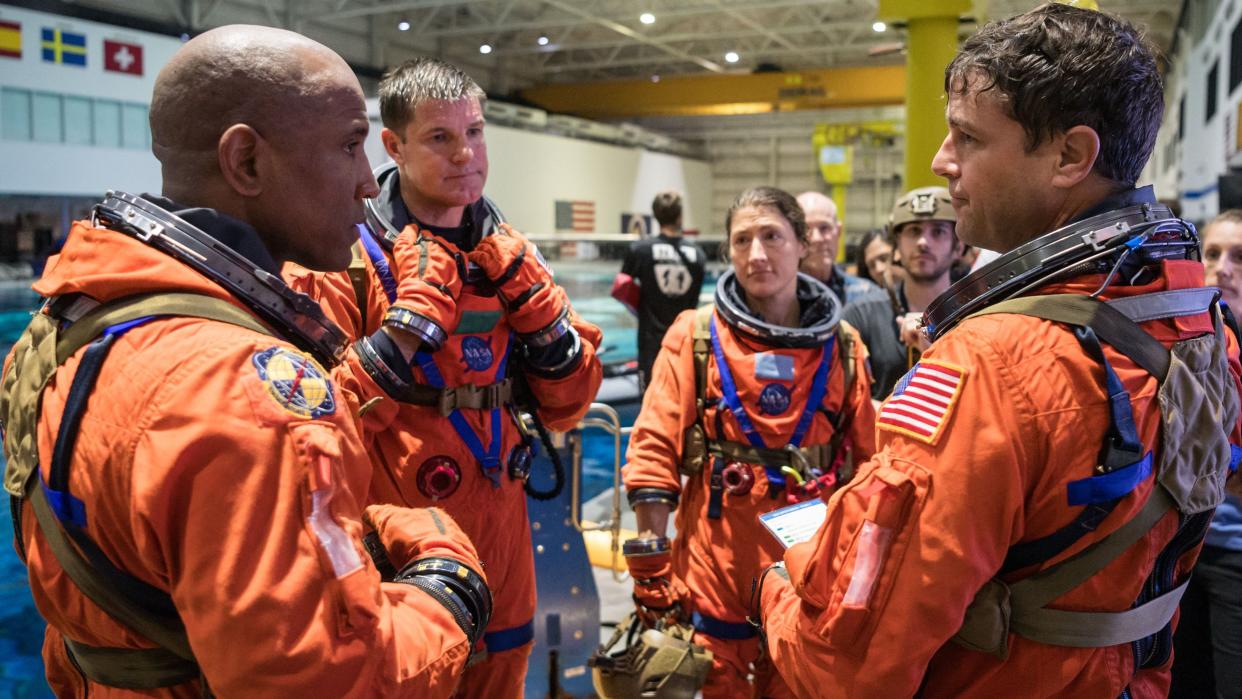  Four astronauts in spacesuits standing in a circle talking to each other. 