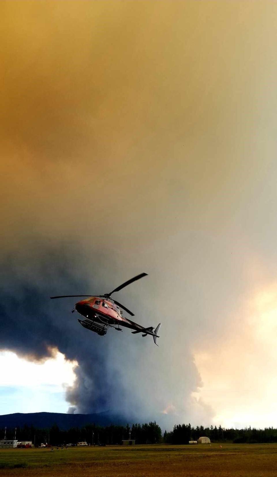 A helicopter hovers at the Mayo, Yukon, airport with the smoke column from the Talbot Creek fire visible in the background, Aug. 6, 2023.
