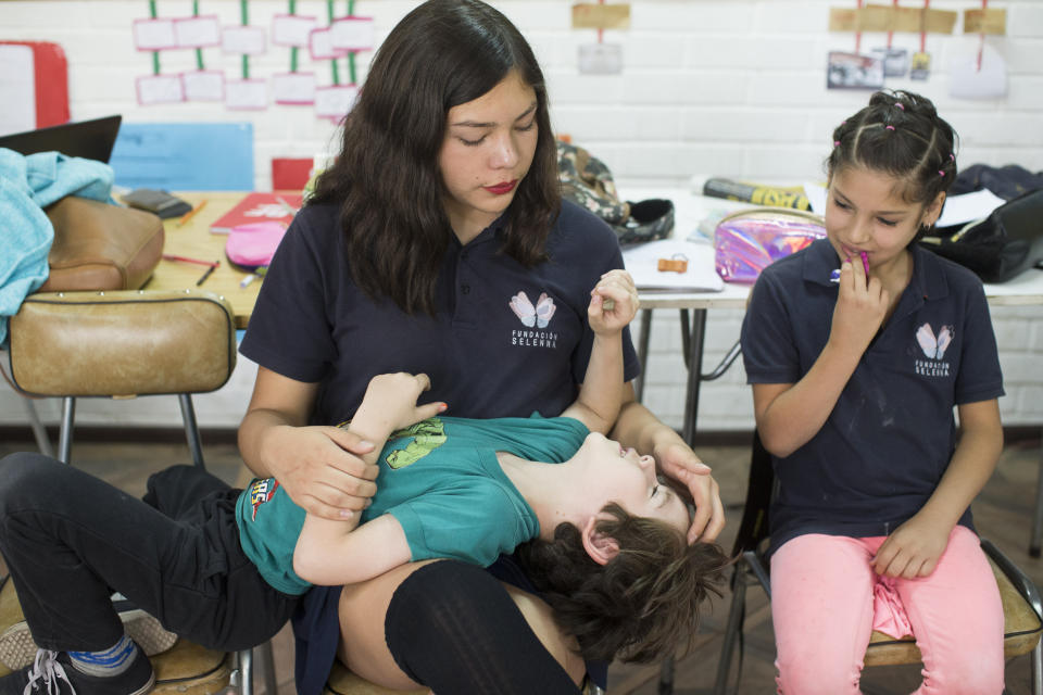 En esta imagen, tomada el 14 de diciembre de 2018, Ángela (arriba izquierda) juega con su compañera de colegio Laura, mientras Violeta (derecha) las observa durante un descanso entre clases en la escuela Amaranta Gómez en Santiago, Chile. Aunque el espacio es reducido, todos los alumnos se ven felices, relajados, participativos y sin temor a hablar delante de sus compañeros. (AP Foto/Esteban Félix)