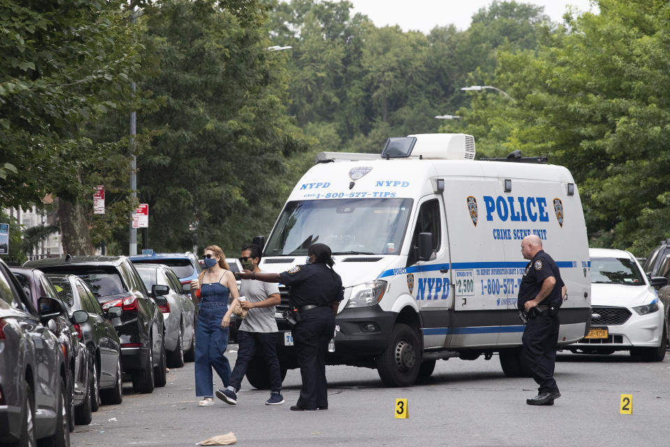 Police direct pedestrians away from the crime scene of a shooting in the Crown Heights neighborhood which left one dead and five injured, Wednesday, July 15, 2020, in the Brooklyn borough of New York. (AP Photo/Mark Lennihan)