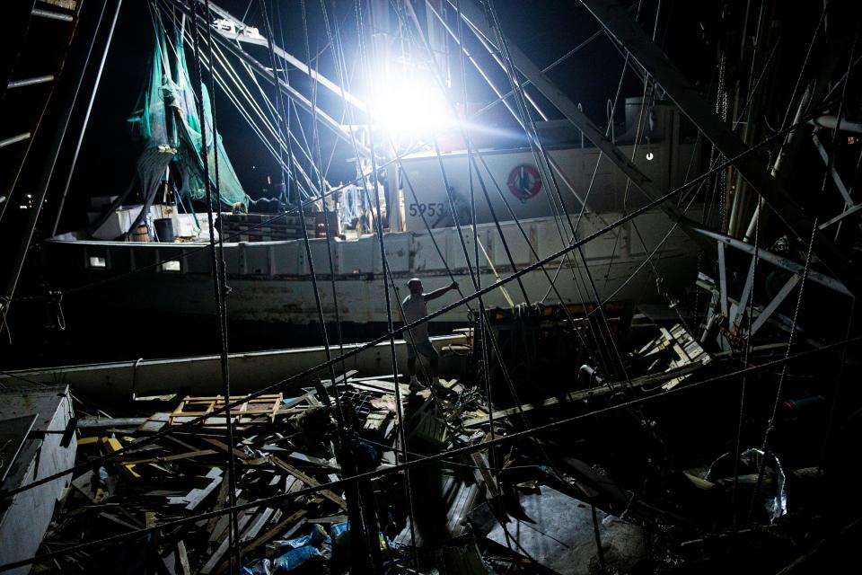 Sean Mynch, a crew member of the shrimp boat Anna, ties her off on the sunken shrimp boat Perseverance on Dec, 1, 2022.  The crew was moving boats to make room for incoming boats. The Anna is one of the few boats that survived Hurricane Ian. The crew was preparing to head out to fish soon. 