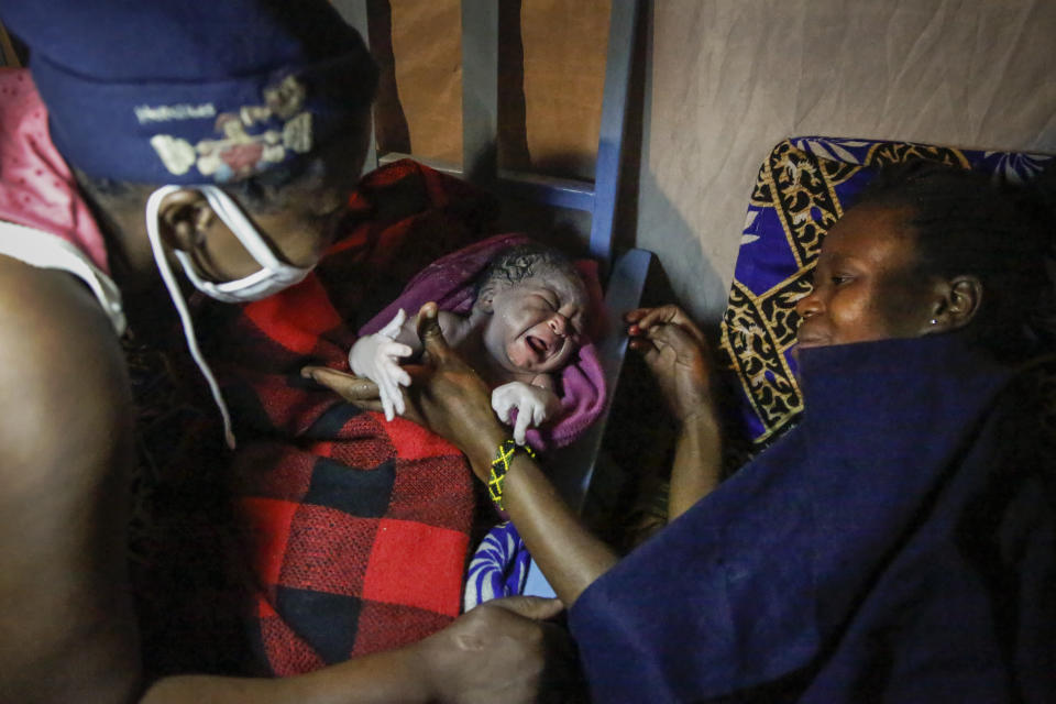 Traditional birth attendant Emily Owino, left, hands over newborn daughter Shaniz Joy Juma, center, to her mother Veronica Atieno, right, after she was born in Emily's one-room house during a dusk-to-dawn curfew, in the Kibera slum of Nairobi, Kenya in the early hours of Friday, May 29, 2020. Kenya already had one of the worst maternal mortality rates in the world, and though data are not yet available on the effects of the curfew aimed at curbing the spread of the coronavirus, experts believe the number of women and babies who die in childbirth has increased significantly since it was imposed mid-March. (AP Photo/Brian Inganga)