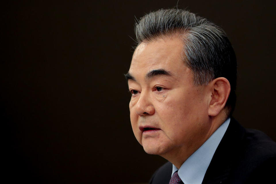 Wang Yi in a suit looking on in front of a black background.
