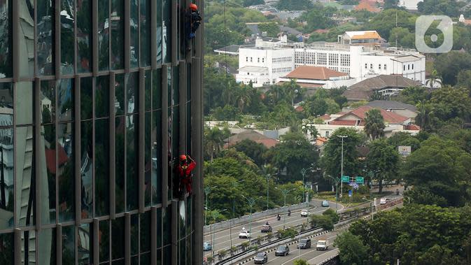 Pekerja bergelantungan membersihkan bagian luar gedung di kawasan Kuningan, Jakarta, Minggu (19/12/2021). Pekerja ini harus bergelantungan dengan seutas tali untuk membersihkan dinding-dinding gedung bertingkat yang tingginya kurang lebih mencapai 150 meter. (Liputan6.com/Johan Tallo)