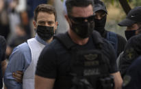 Helicopter pilot Babis Anagnostopoulos, left, escorted by police officers arrives to the prosecutor's office at a court to give evidence, in Athens, Tuesday, June 22, 2021. Anagnostopoulos was charged last Friday with the murder of his British-Greek wife, Caroline Crouch, 20, whose death he had initially claimed was caused by burglars during a brutal invasion of their home on the outskirts of Athens. (AP Photo/Petros Giannakouris)