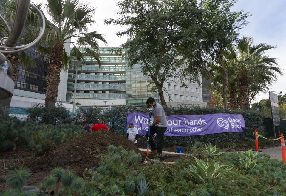 A sign posted outside the Cedars-Sinai Medical Center reads: "Wash your hands, Take care of each other," as maintenance workers dig a trench in Los Angeles Thursday, Jan. 7, 2021. California health authorities reported Thursday 583 new deaths and a record two-day total of 1,042. The state has deployed 88 refrigerated trailers, up from 60 a few weeks ago, for use as makeshift morgues, mostly in hard-hit Southern California. (AP Photo/Damian Dovarganes)