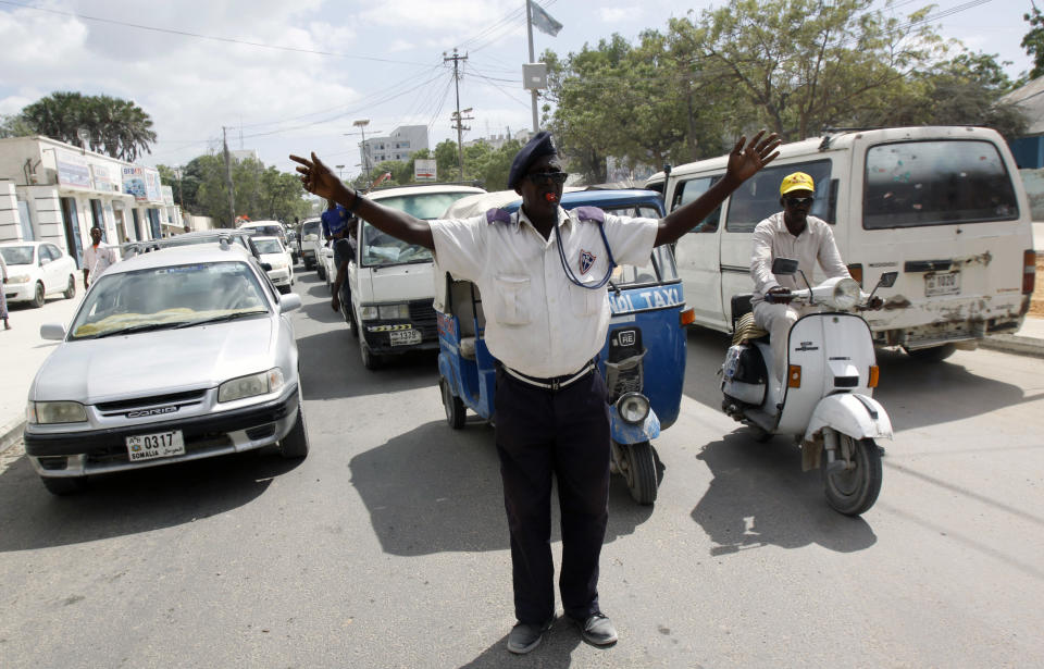 In this photo dated Sunday, Dec. 8, 2013, A Somali traffic police officer stands at a Mogadishu junction in a vain effort to regulate cars and traffic movements in Mogadishu, Somalia. The traffic police officer yells, waves his arms and blows his whistle for car drivers to obey the traffic signals but many don't notice the signals. Many of the cars do not stop, and angered, the police officer steps into the middle of the road, as other cars encroach further, obstructing another lane of traffic and creating a scene of gridlock and the unarmed officer is forced to allow more cars to run the red light in order to clear the congestion. (AP Photo/Farah Abdi Warsameh)