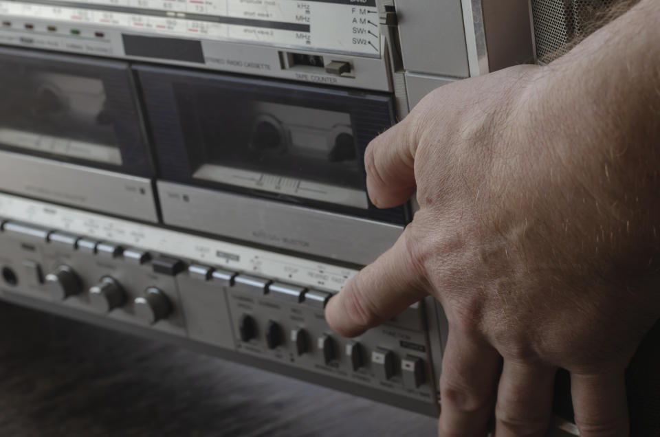 Close-up of a hand pressing a button on a vintage cassette player with tuner and knobs visible