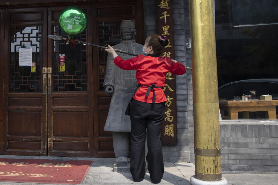 A waitress wearing a mask to curb the spread of the coronavirus uses the pike of a terra-cotta warrior sculpture to remove a balloon as she spreads to open a restaurant for business in Beijing on Wednesday, July 8, 2020. (AP Photo/Ng Han Guan)