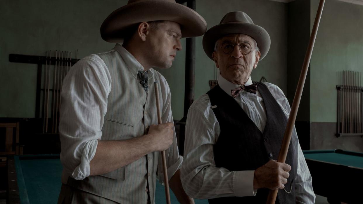 leonardo dicaprio and robert de niro in character for killers of the flower moon, the men stand inside a pool hall with serious looks on their faces, each holds a pool cue and wears a cowboy hat, vest, collared shirt and tie